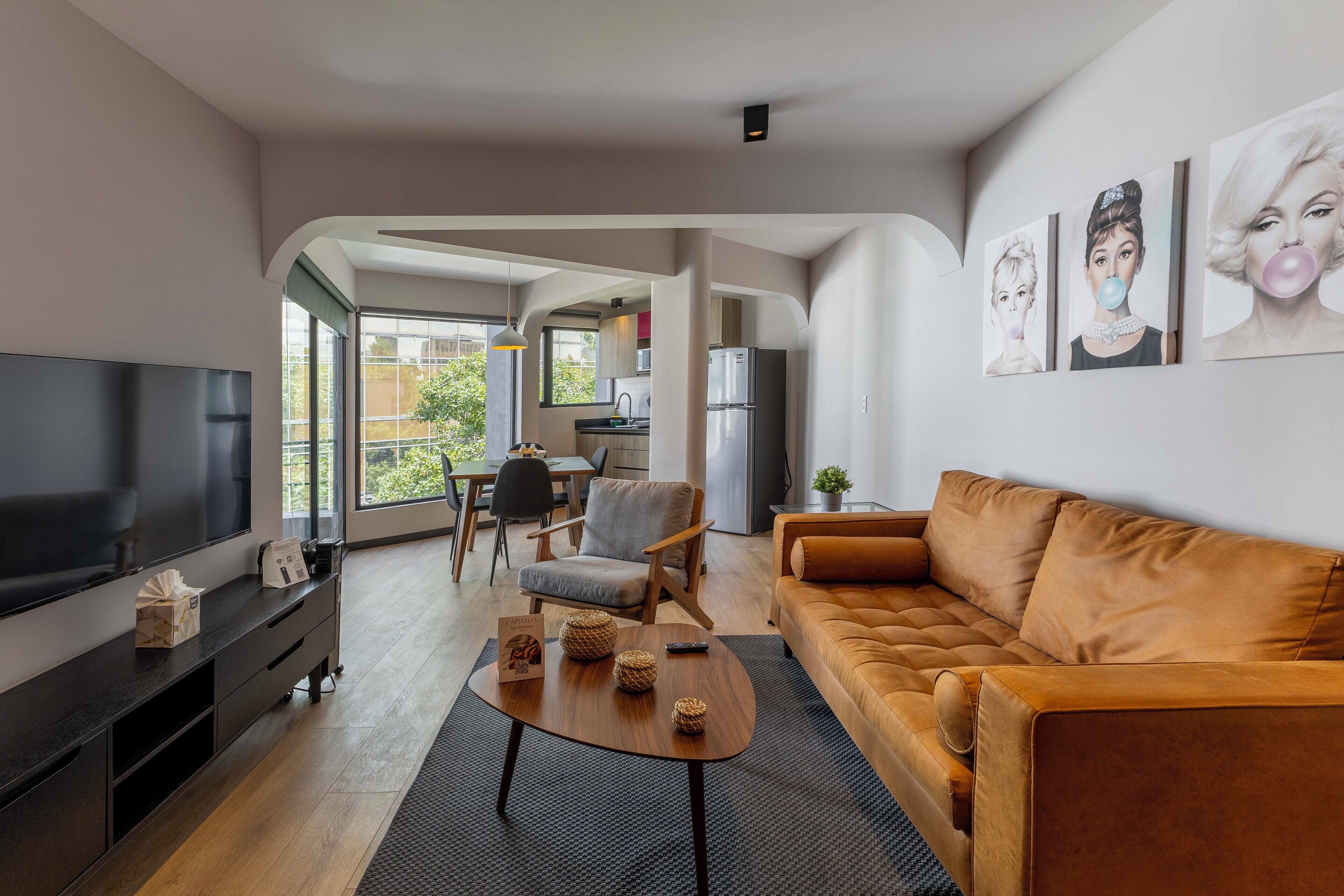 A modern living room with a flat-screen TV, a brown sofa, a wooden coffee table, and a dining area with a chair and table.