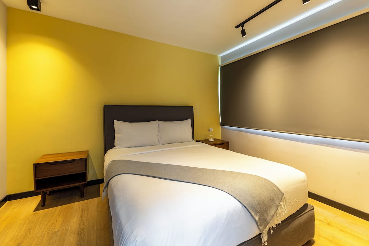 A modern hotel room with a bed, bedside tables, and a large window.