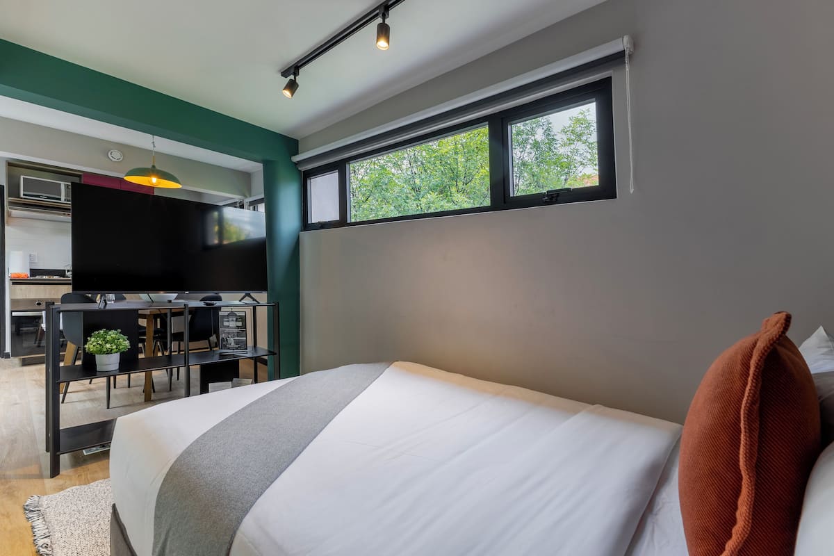 A modern bedroom with a bed, a desk, and a television in the adjacent room.