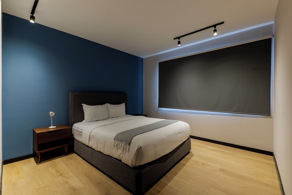 A modern bedroom with a large bed, a nightstand, a bedside lamp, and a large window.