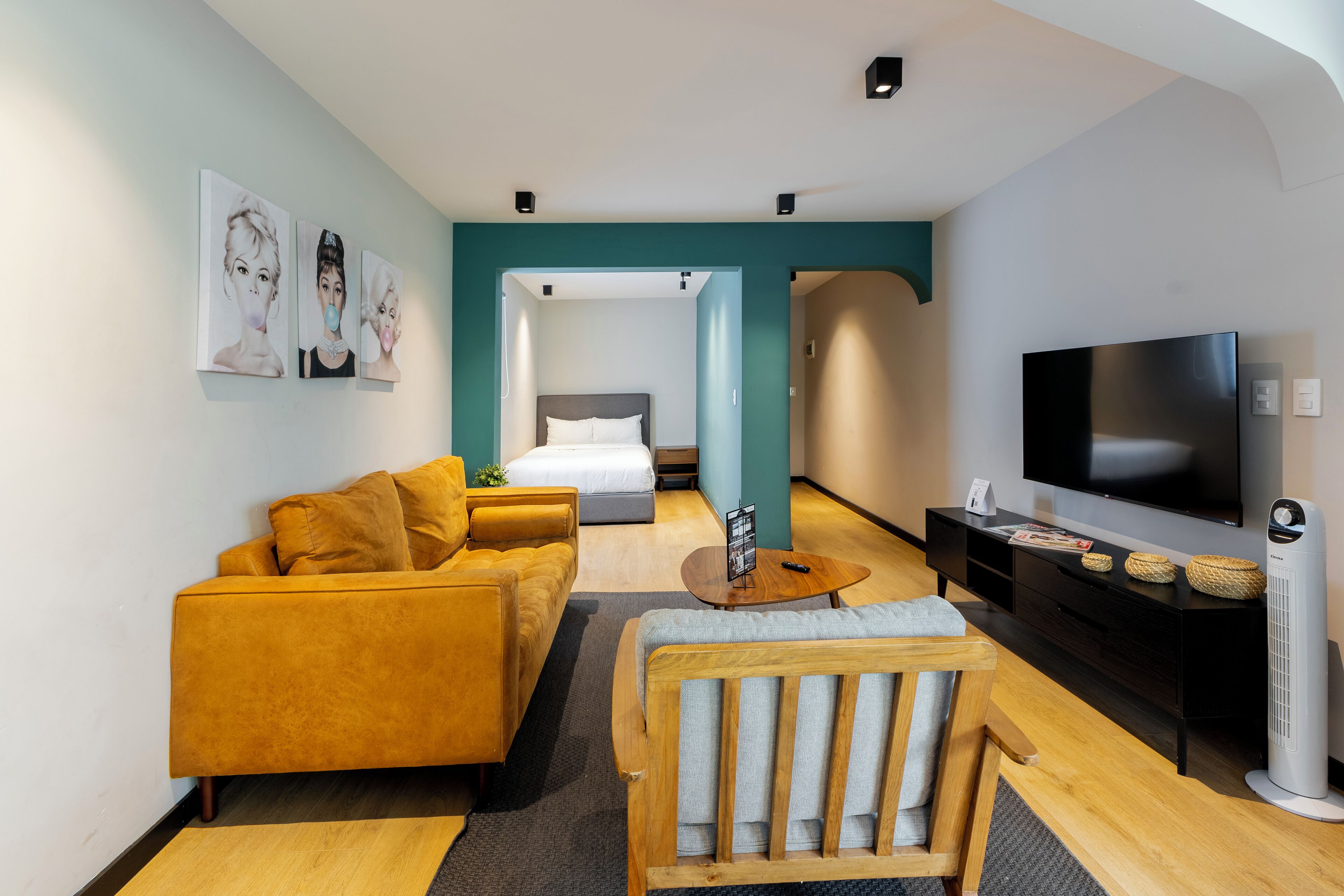 A modern hotel room with a sofa, armchair, TV, and a bed in the background.