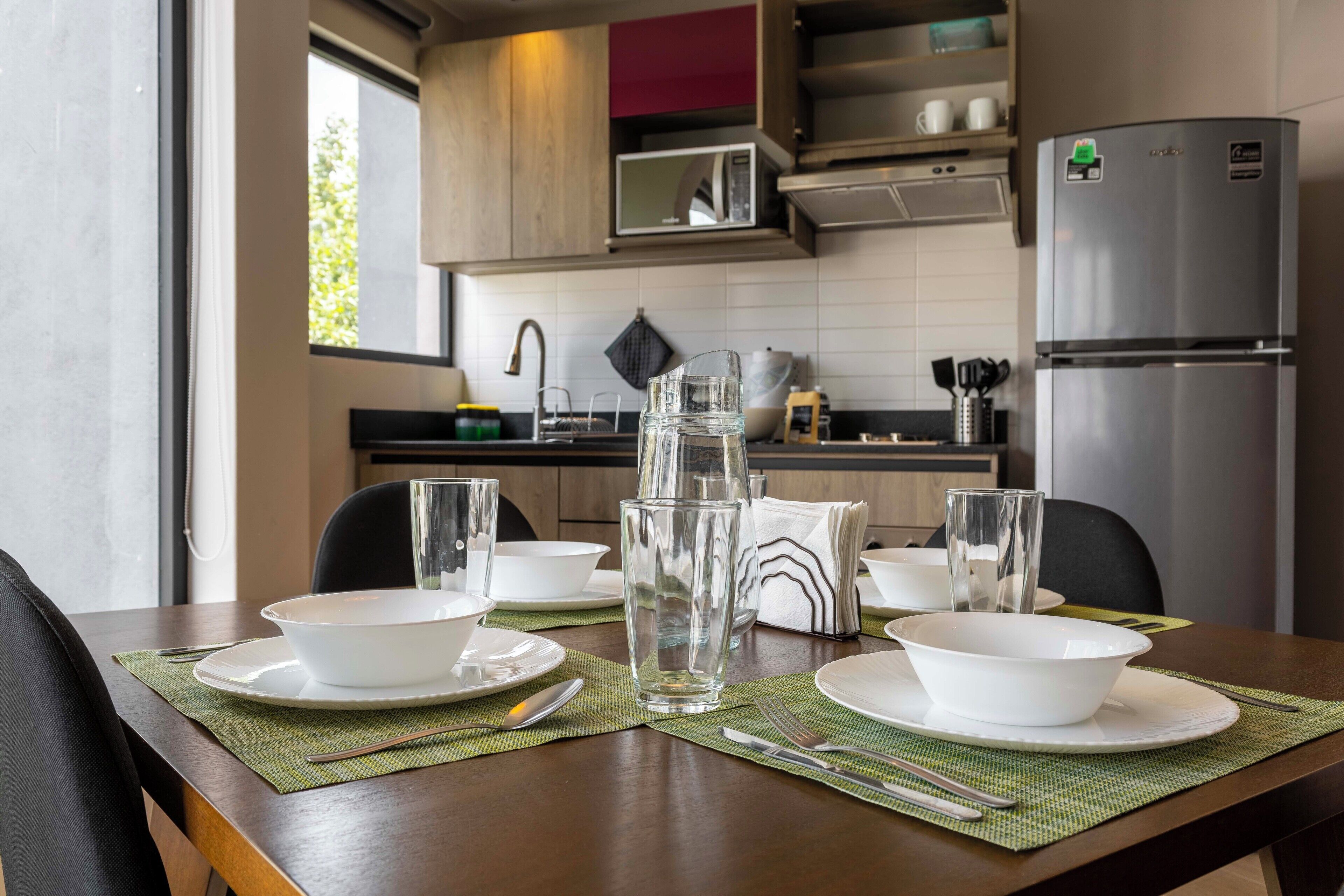 A modern kitchen with a dining table set for four, equipped with white bowls, plates, and cutlery.