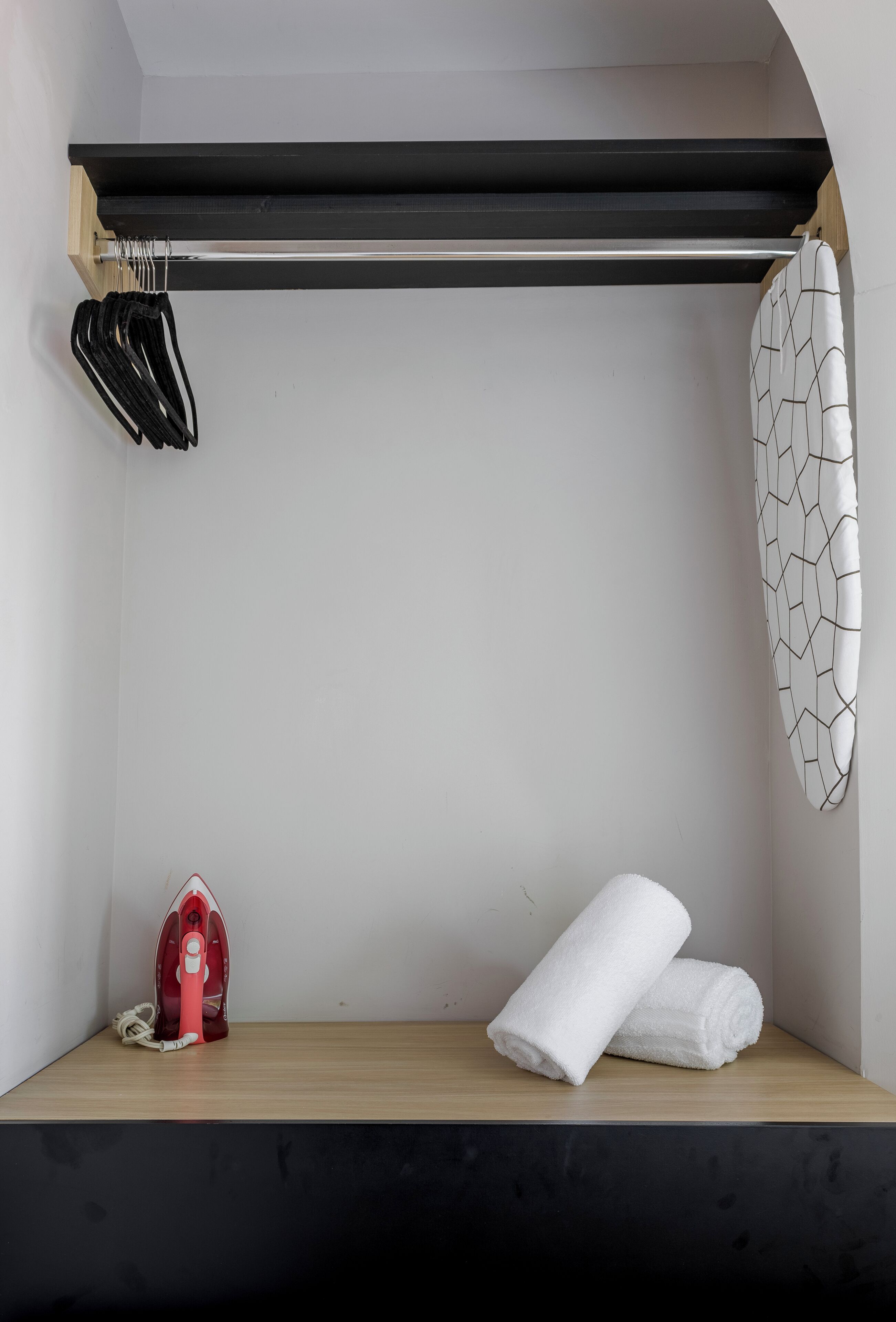 A small, neatly organized bathroom with a wooden shelf, a towel, an iron, and a towel rack.
