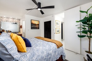 Un dormitorio con cama, ventilador de techo, planta y vista al exterior.