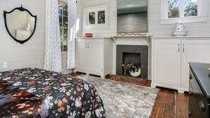 Een slaapkamer met een bed, een open haard, een spiegel en een raam.