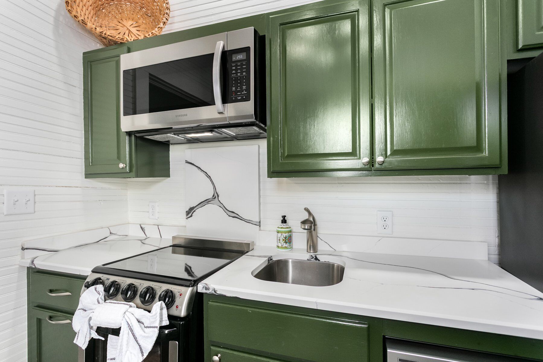 A kitchen with green cabinets, a stainless steel sink, a microwave, and a stove.