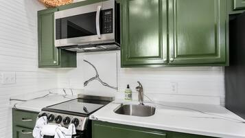A kitchen with green cabinets, a stainless steel sink, a microwave, and a stove.