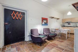 Une pièce avec deux chaises, une table, une porte noire et un coin cuisine.