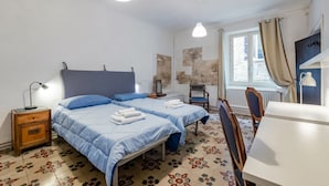 Ein Schlafzimmer mit zwei Betten, einem Sessel, einem Tisch und einem Fenster mit Vorhängen.