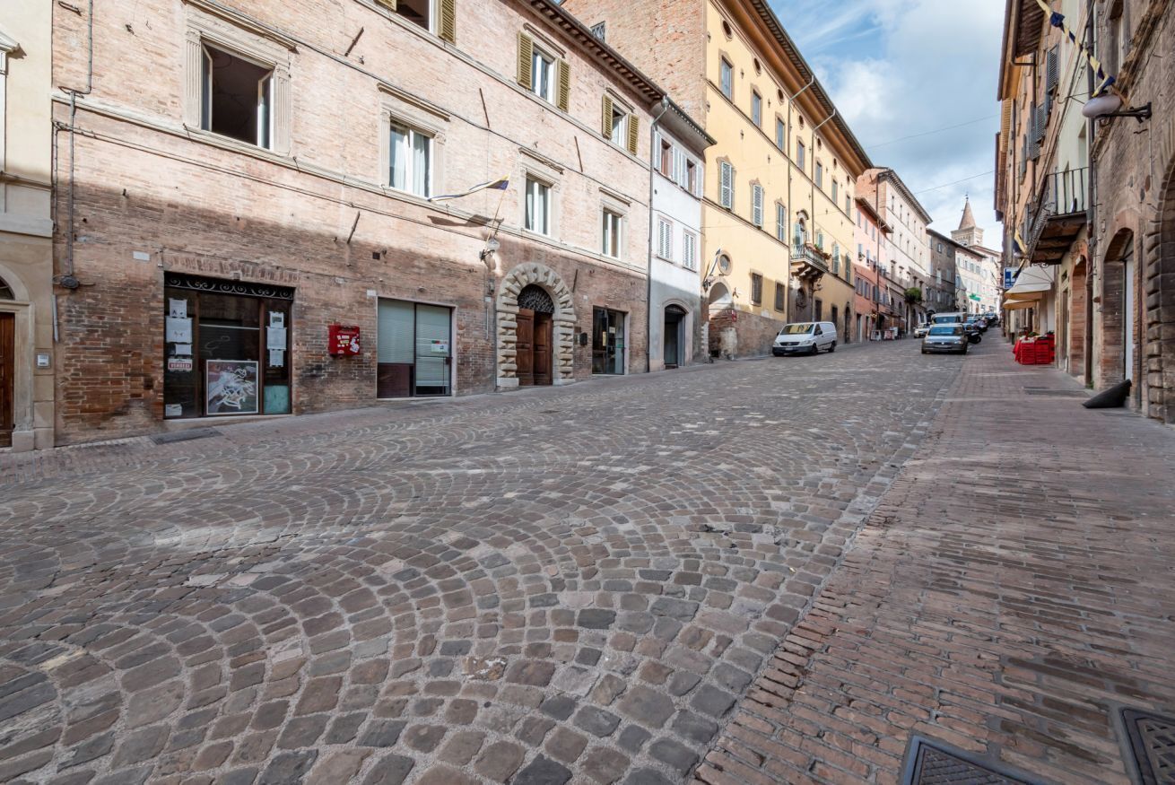 Une rue pavée bordée de bâtiments historiques, dont certains abritent des boutiques et arborent des enseignes.