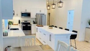 Una cucina moderna con mobili bianchi, un'isola centrale e un'area da pranzo con un tavolo lungo e sedie.