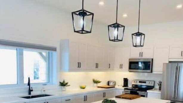 Una cucina moderna con un'isola grande, sgabelli neri e luci a sospensione.