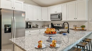 A modern kitchen with white cabinets, stainless steel appliances, a granite countertop, and a fruit cake centerpiece. - Historic Downtown - close to beaches - firepit - playground - pet friendly (St. Augustine)