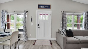 A modern living room with a dining area, a sofa, and a door with a 'happy place' sign. - Historic Downtown - close to beaches - firepit - playground - pet friendly (St. Augustine)