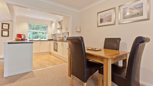 A modern kitchen with white cabinets, a wooden dining table, and black chairs. There are two framed pictures on the wall. - Herdwick Place, spacious cottage for 4 in spectacular Langdale Valley (Great Langdale)