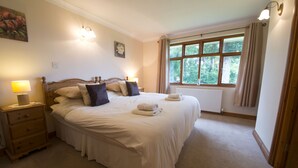 A neatly arranged bedroom with a large bed, bedside lamps, a window with curtains, and a radiator. - Low How Cottage, Coniston, spacious single level, 4 bedroom cottage sleeping 10 (Coniston)