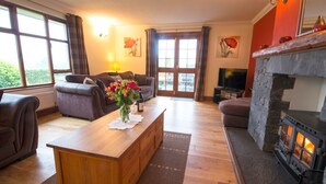 A cozy living room with a fireplace, a sofa, a coffee table with flowers, and a television. - Low How Cottage, Coniston, spacious single level, 4 bedroom cottage sleeping 10 (Coniston)