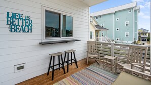 A covered porch with a window, two stools, a bench, and a colorful striped rug. - ‘B’ by the Sea: comfort and style, essentials included! (Carolina Beach)