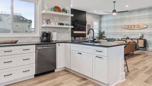 A modern kitchen with white cabinetry, a large island, and a view of the ocean through the window. - ‘B’ by the Sea: comfort and style, essentials included! (Carolina Beach)