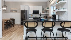 A modern kitchen with white cabinets, a black refrigerator, and a central island with bar stools. - ‘B’ by the Sea: comfort and style, essentials included! (Carolina Beach)