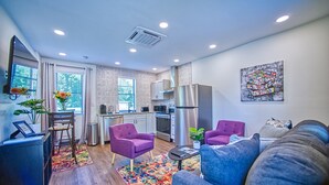 A modern apartment with a kitchen, dining area, and living room. It features a large window, a refrigerator, a microwave, and a sofa. - 1930s Cape Cod Bungalow at Firmstone Manor (Clifton Forge)