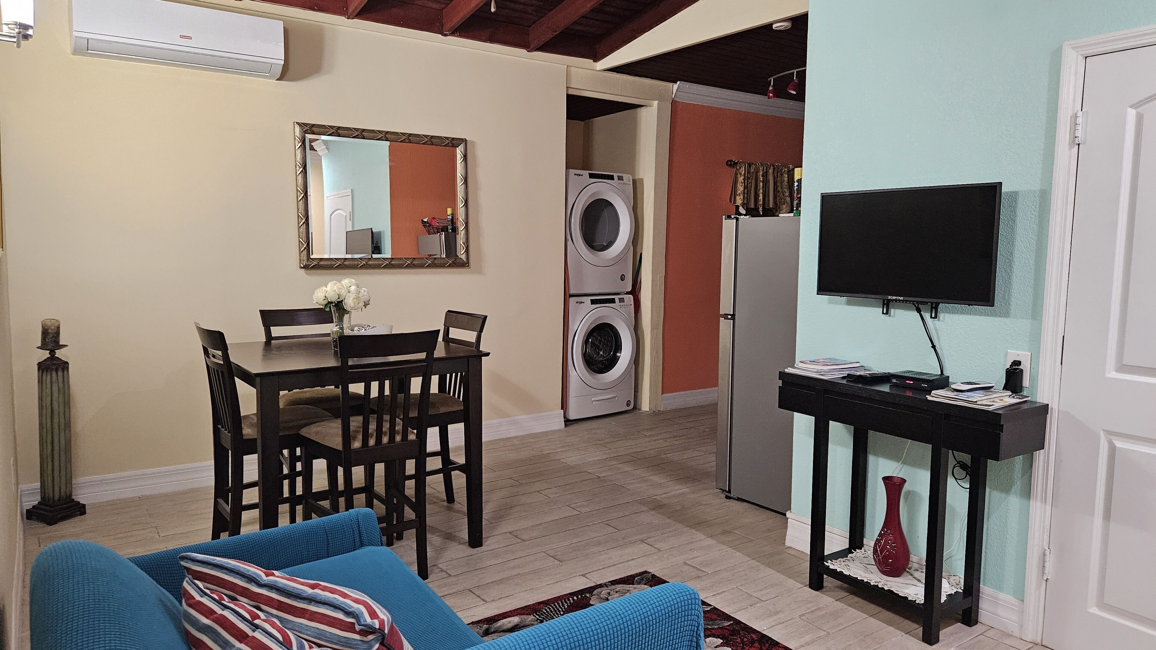 En kompakt bolig med spiseplads, sofa, tv, vaskemaskine og køleskab.