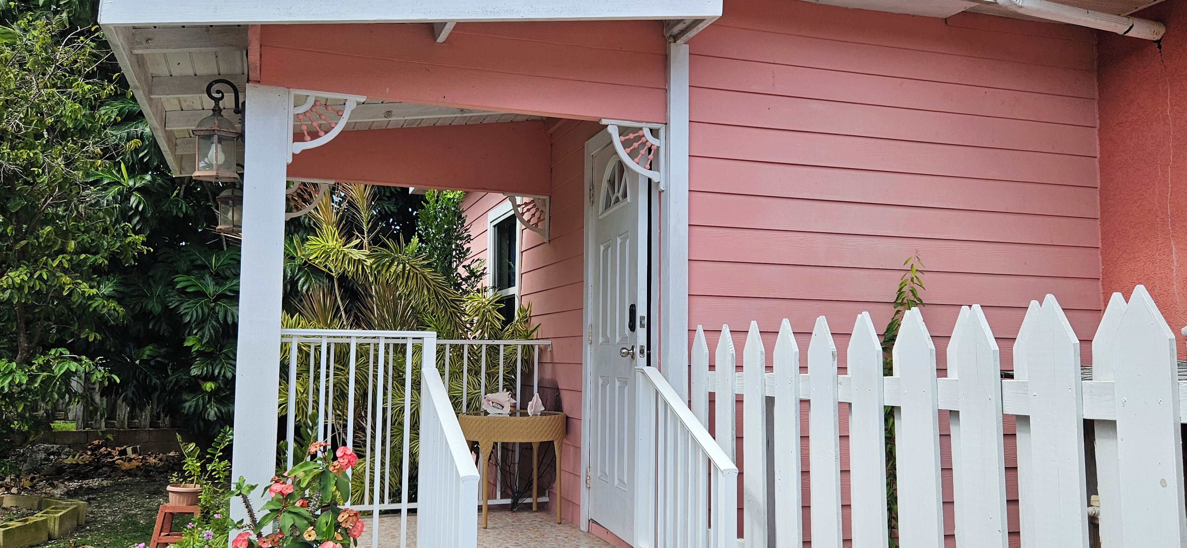 Ein pinkfarbenes Haus mit weißem Zaun, einer Veranda und einem kleinen Garten.