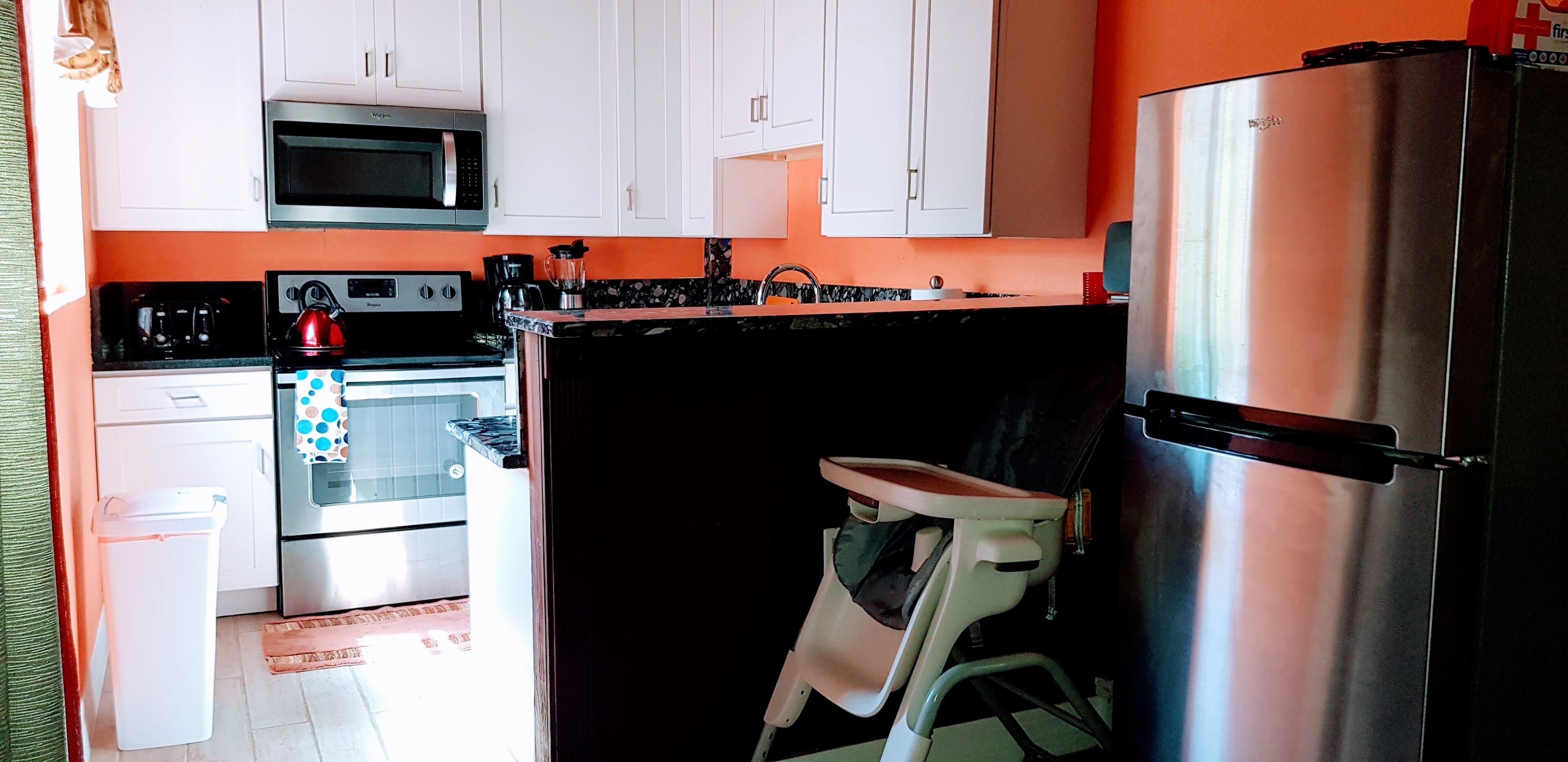 A compact kitchen with white cabinets, a stainless steel refrigerator, a microwave, a stove, and a sink.
