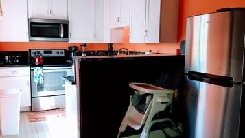 A compact kitchen with white cabinets, a stainless steel refrigerator, a microwave, a stove, and a sink.