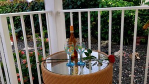 Et rundt glasbord med en flaske og to glas, omgivet af et hvidt hegn og grøn vegetation.