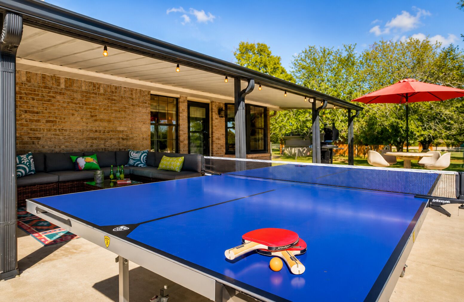 A ping pong table with a net, a red table tennis paddle, and a yellow ball.