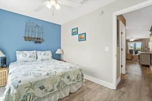 Een slaapkamer met een bed, een plafondventilator, een blauw accent op de muur en een deur naar een balkon.