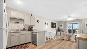 A kitchen with white cabinets, a coffee maker, and a dining area with white chairs. - Dog Heaven · Pet-Friendly Beach·Pools & Pickleball (Port St. Joe)