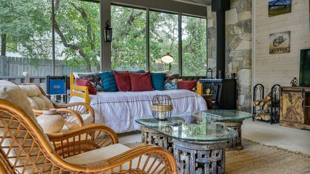 Una sala de estar acogedora con una cama grande, muebles de mimbre, una mesa de centro de vidrio y una chimenea de piedra.
