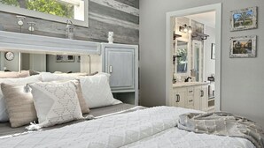 Un dormitorio con una cama grande, un tocador, una cómoda y un ventanal con vista a árboles.