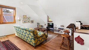 Un salon avec un canapé à motifs, un plancher en bois, un téléviseur et un coin cuisine doté d’un comptoir et de tabourets.