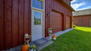 Une grange rouge avec une porte blanche, deux portes de garage et une pelouse bien entretenue où l’on peut voir des citrouilles et un nichoir.