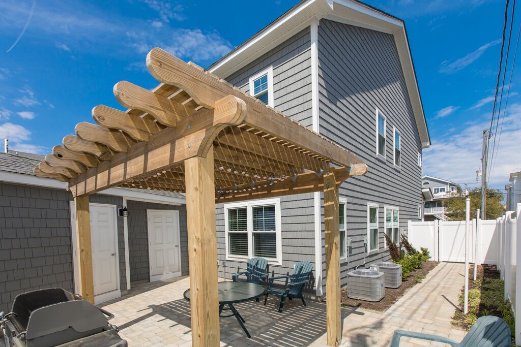 A covered patio with a wooden pergola, a barbecue grill, and outdoor seating.