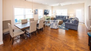 A spacious living room with a wooden floor, a dining area with a table and chairs, a sofa set, and a TV mounted on the wall. - Beach Music - North End VB (Virginia Beach)