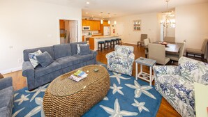 A modern living room with a grey sofa, a round ottoman, and a patterned rug. - Beach Music - North End VB (Virginia Beach)