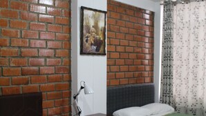A room with two beds, a brick wall, a painting, a nightstand, and a lamp. - Hospedaje Las Parraz (Subtanjalla)