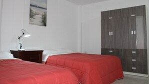 A bedroom with two beds, a nightstand, a lamp, a wardrobe, and a painting on the wall. - Hospedaje Las Parraz (Subtanjalla)