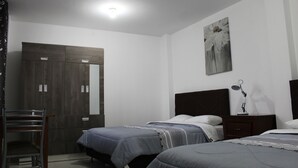 A bedroom with two beds, a wooden wardrobe, a desk, and a nightstand with a lamp. - Hospedaje Las Parraz (Subtanjalla)