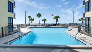 En swimmingpool med utsikt över stranden, omgiven av palmer och en klar himmel.