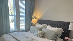 A bedroom with a large bed, a ceiling fan, a nightstand with a lamp, and a window with curtains. - Walk to the square and the grove! This 2BR 2BA is the perfect location.  (Oxford)