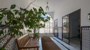 A corridor with a wooden bench, tiled walls, a potted plant, and a view through a glass door. - VEGALUZ - Cosy flat in the centre of Jerez with free Wifi (Jerez de la Frontera)