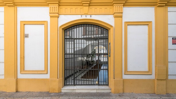 A building entrance with a large arched metal gate, a yellow and white facade, and a staircase leading to the entrance. - VEGALUZ - Cosy flat in the centre of Jerez with free Wifi (Jerez de la Frontera)