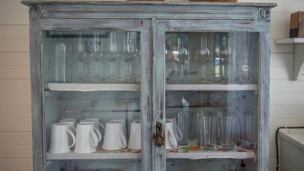 Un aparador antiguo con puertas de cristal, que contiene tazas de cerámica blanca y cristalería transparente.