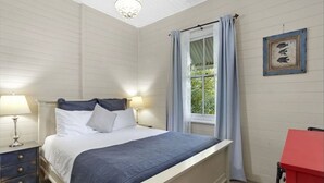 Une chambre à coucher comprenant un lit, deux tables de chevet, une commode, une fenêtre avec des rideaux et un tableau accroché au mur.