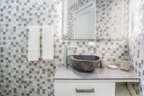Features a sleek, minimalist design with a large round sink and mosaic tile walls.